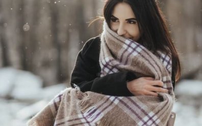 Mujer joven envuelta en una bufanda de cuadros entre la nieve