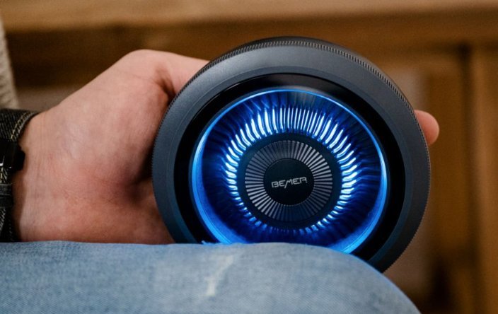 Mano sujetando un dispositivo circular BEMER con luz azul iluminada en el centro