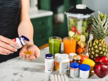 Mujer sirviéndose suplementos en la mano junto a batidora con frutas y verduras