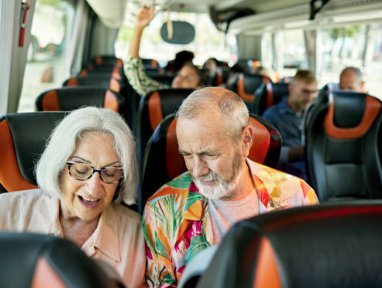 Pareja mayor mirando un móvil juntos sentados en un autobús turístico